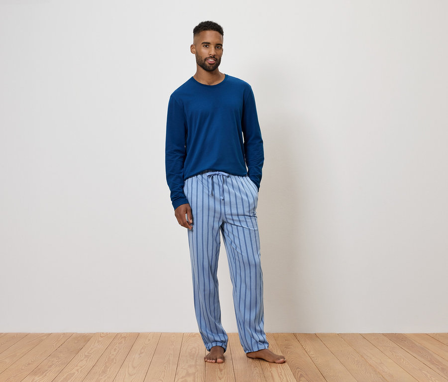 Muž v modrom pyžame s dlhým rukávom a pruhovanými nohavicami.