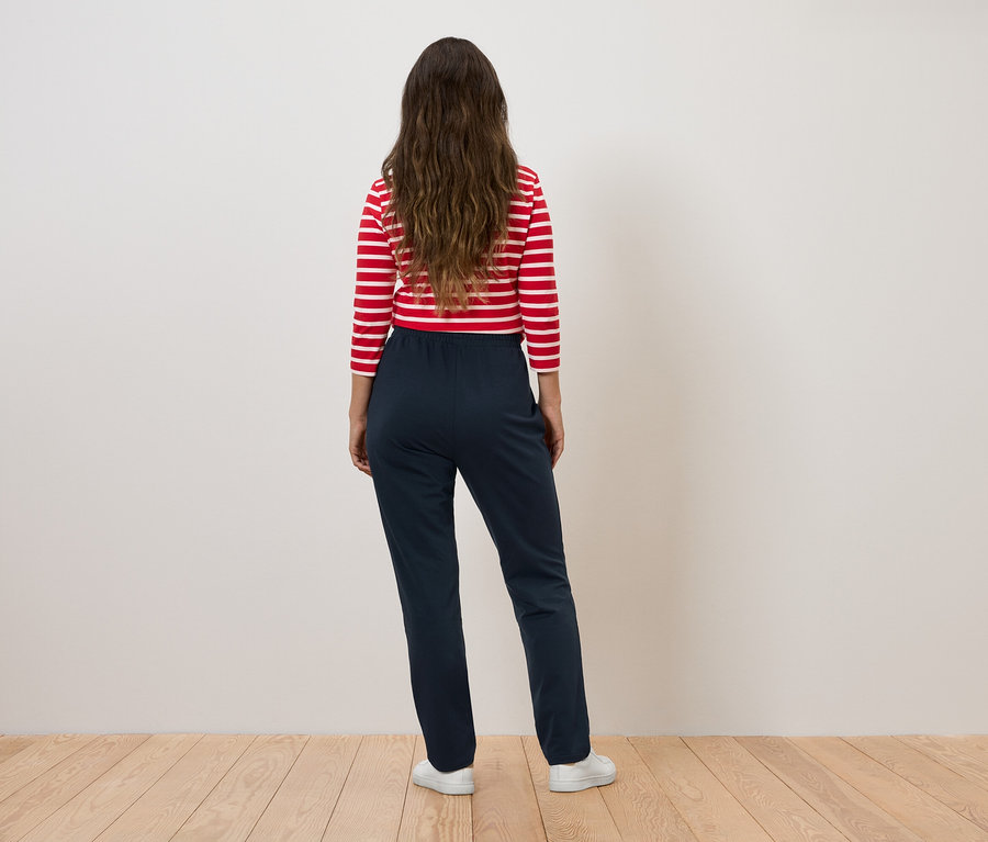 Žena v červeno-bielom pruhovanom tope a tmavomodrých nohaviciach stojí chrbtom k fotoaparátu.