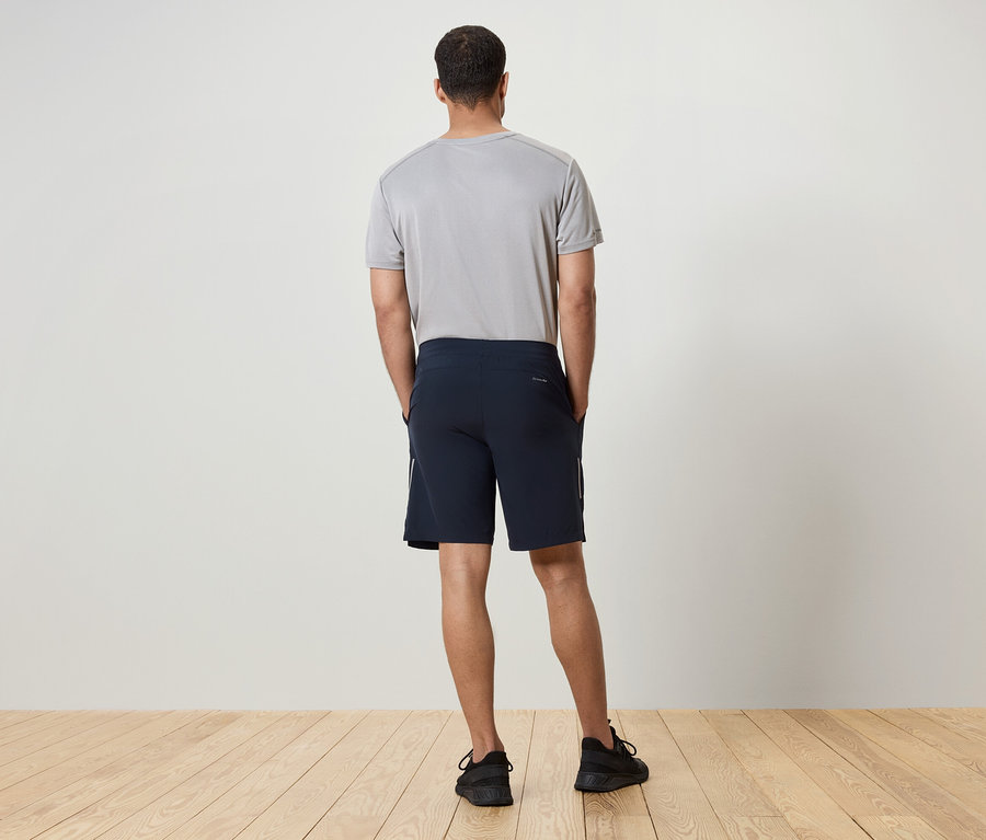 Muž chrbtom k fotoaparátu má na sebe sivé tričko, tmavomodré šortky a čierne tenisky.