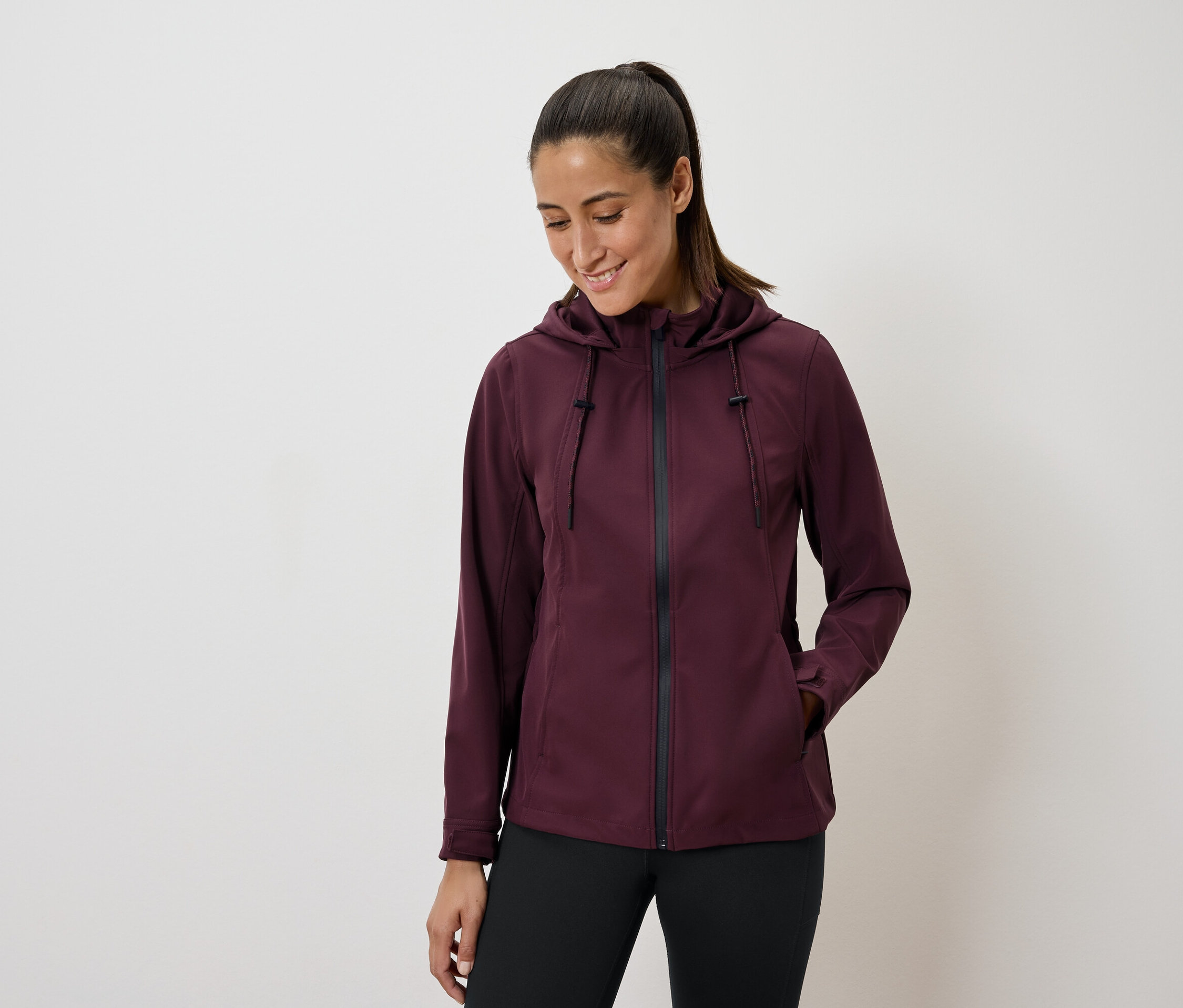 Žena v bordovej bunde s kapucňou a čiernych legínach.