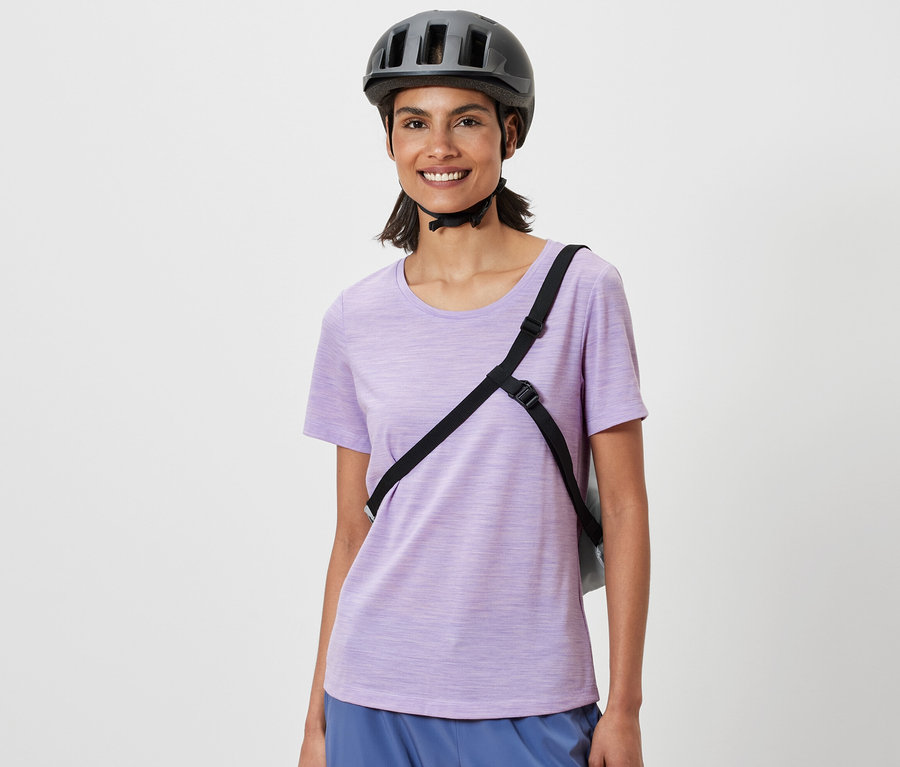 Usmievajúca sa žena s cyklistickou helmou a nákupnou taškou na bicykel cez rameno.