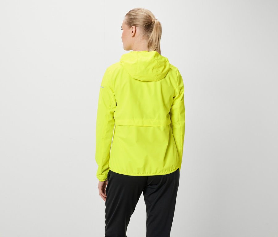 Zozadu je vidieť ženu s blond vlasmi stiahnutými do copu, má na sebe neónovo žltú bundu s kapucňou a čierne nohavice.