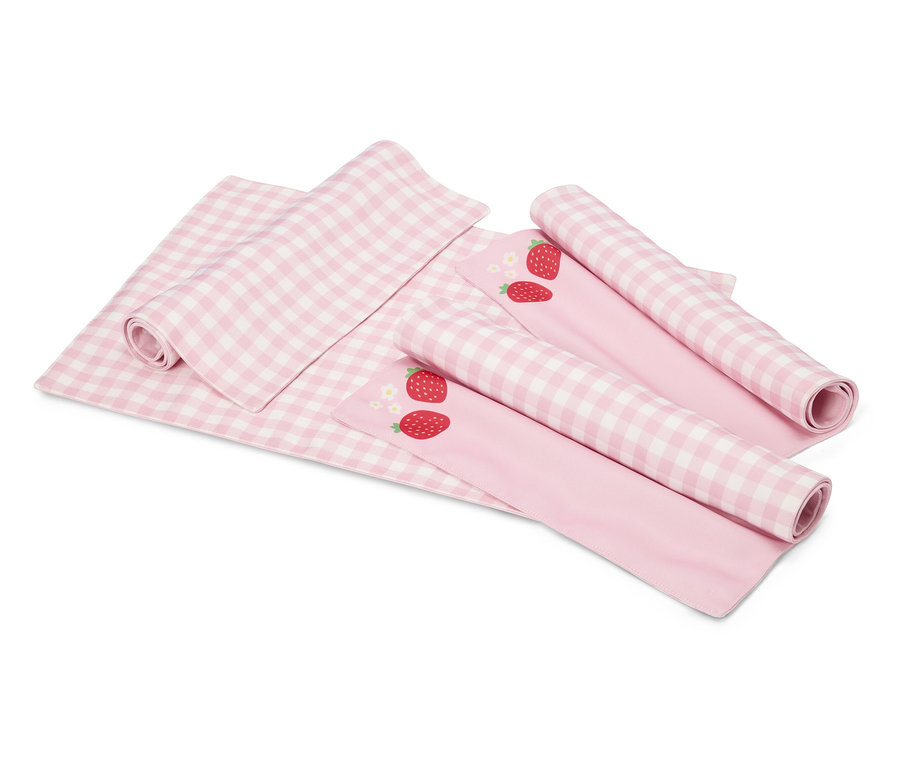 Na bielom pozadí leží ružovo-biela kockovaná deka a dve ružové látky s motívmi jahôd, čiastočne zrolované.