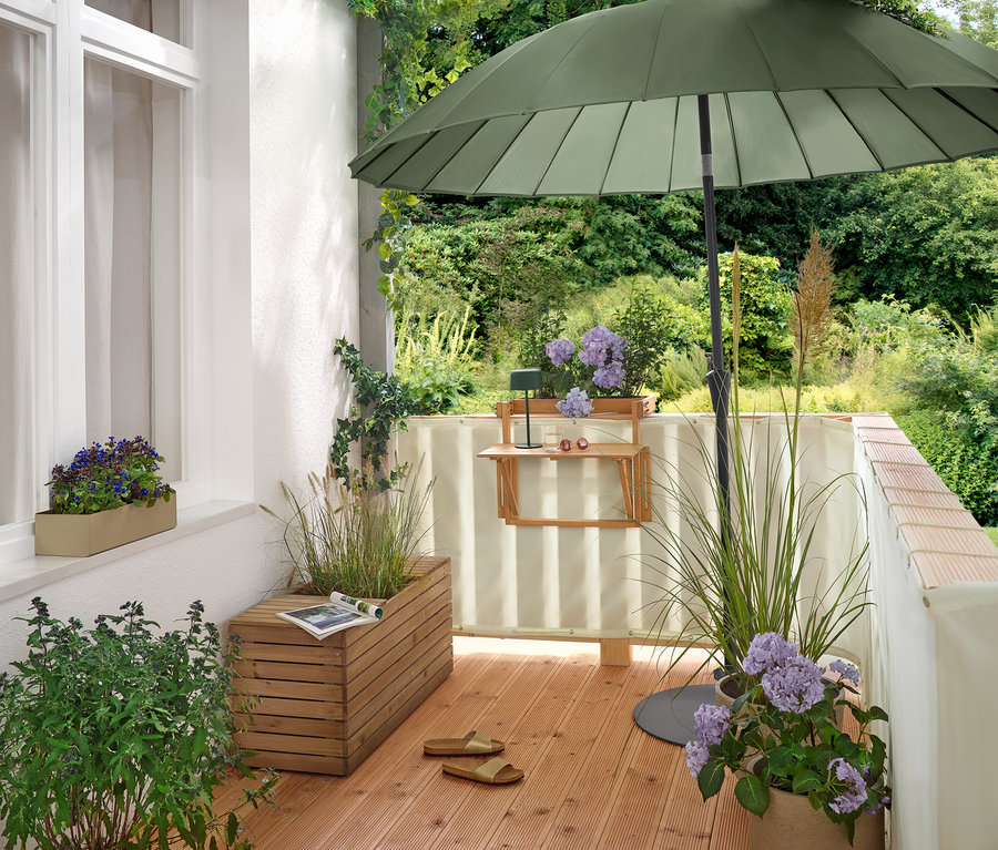 Na balkóne stojí zelený slnečník Leco Shanghai (Ø 270 cm) v plochom stojane Leco (Ø cca 60 cm).