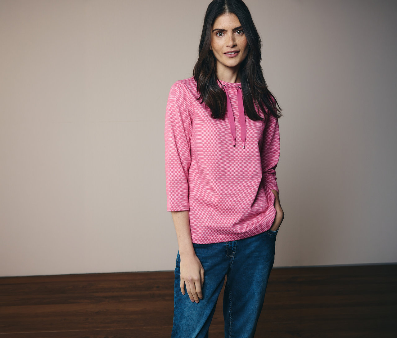 Žena v džínsoch a ružovej mikine CECIL s kapucňou a 3/4 rukávmi, s rukou vo vrecku.