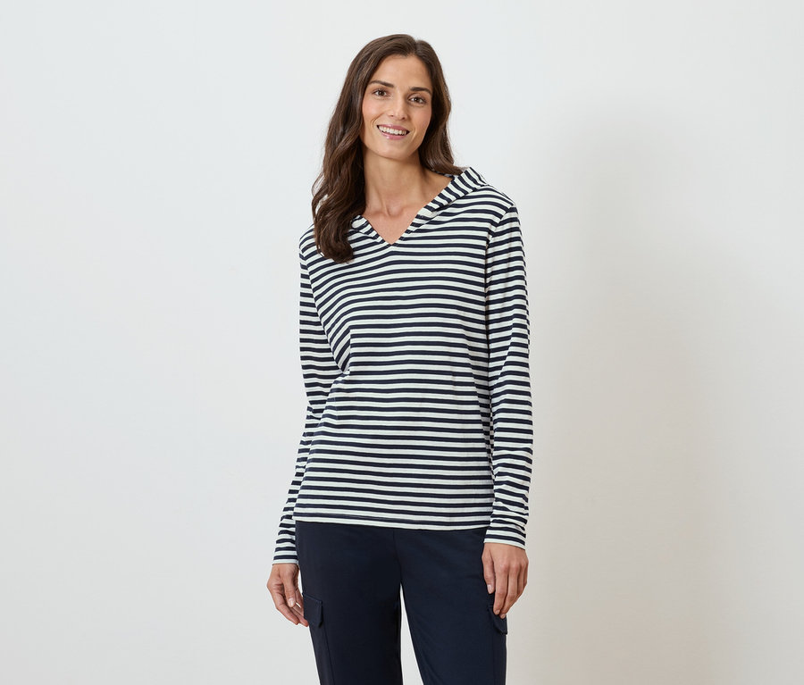 Žena má na sebe pásikavý top s dlhým rukávom a kapucňou a tmavomodré nohavice.