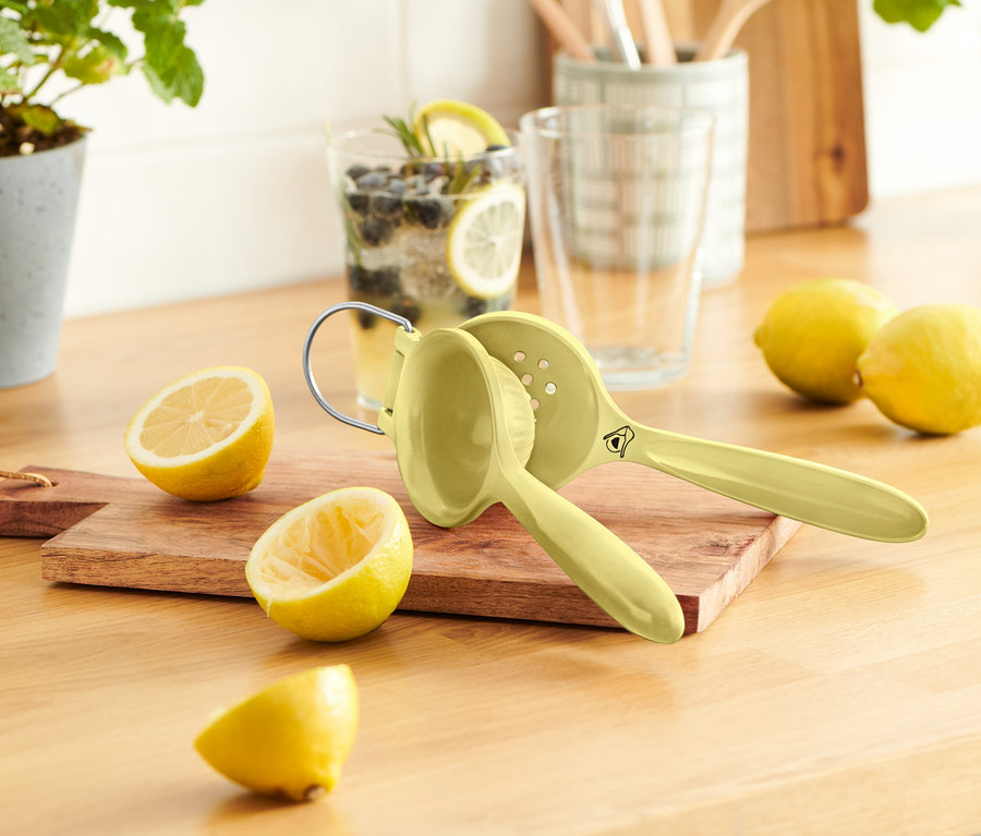 Na drevenom stole je niekoľko citrónov, odšťavovač citrónov a pohár limonády.