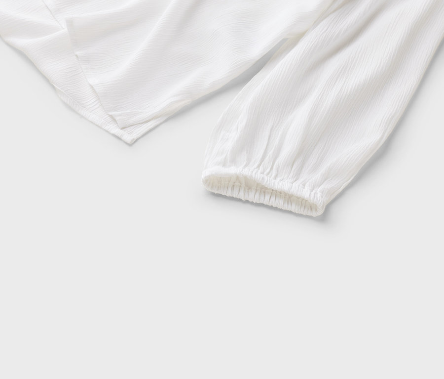 Detailný pohľad na bielu blúzku s dlhými rukávmi a nariasenými manžetami na bielom pozadí.