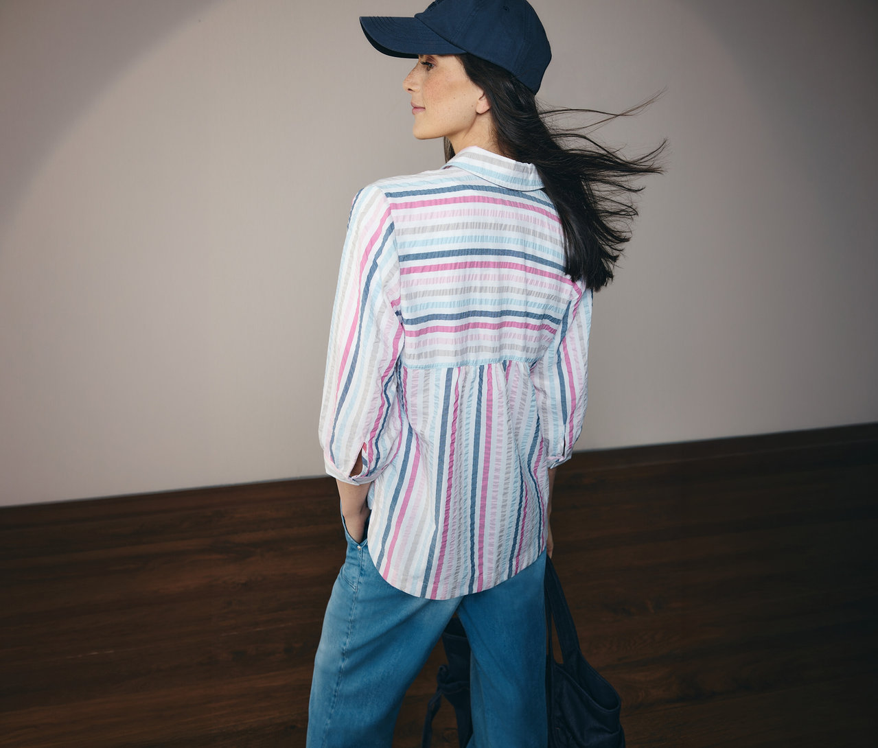 Žena v džínsoch a modro pruhovanej košeľovej blúzke CECIL a šiltovke, pohľad zozadu.