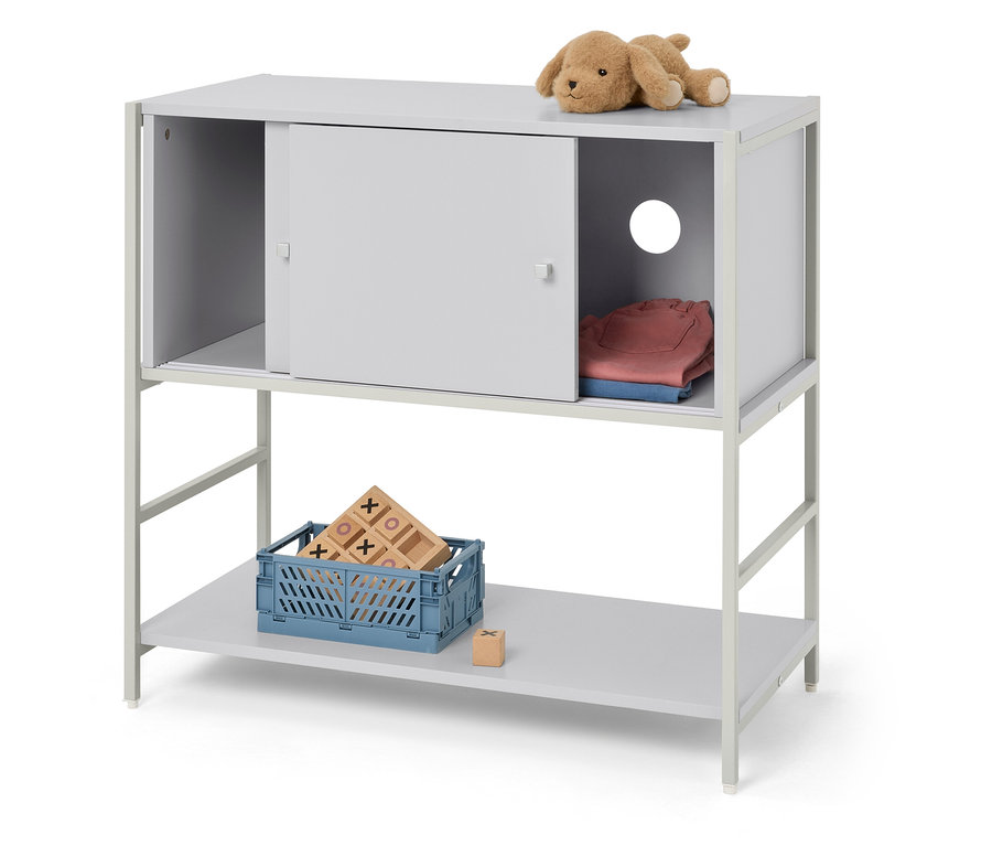 Sivý regál s dvoma policami. Na hornej polici je plyšové zvieratko a oblečenie, na dolnej polici je modrá debna s hračkami.