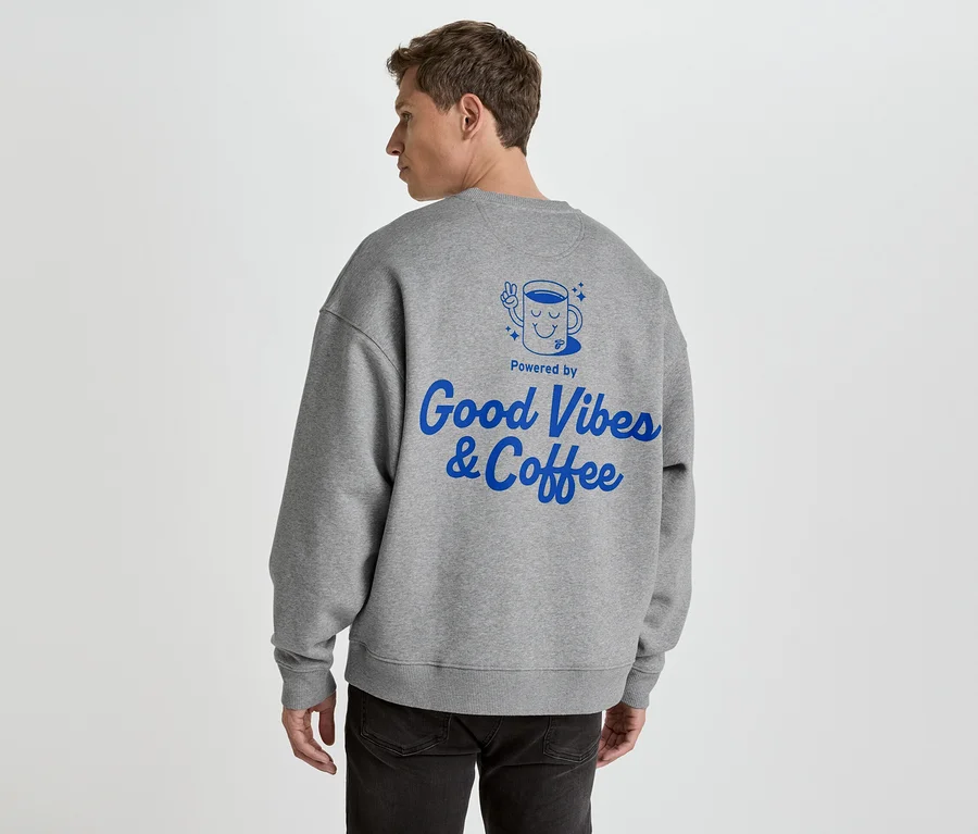 Muž zozadu v šedej mikine s modrou potlačou 'Good Vibes & Coffee'.
