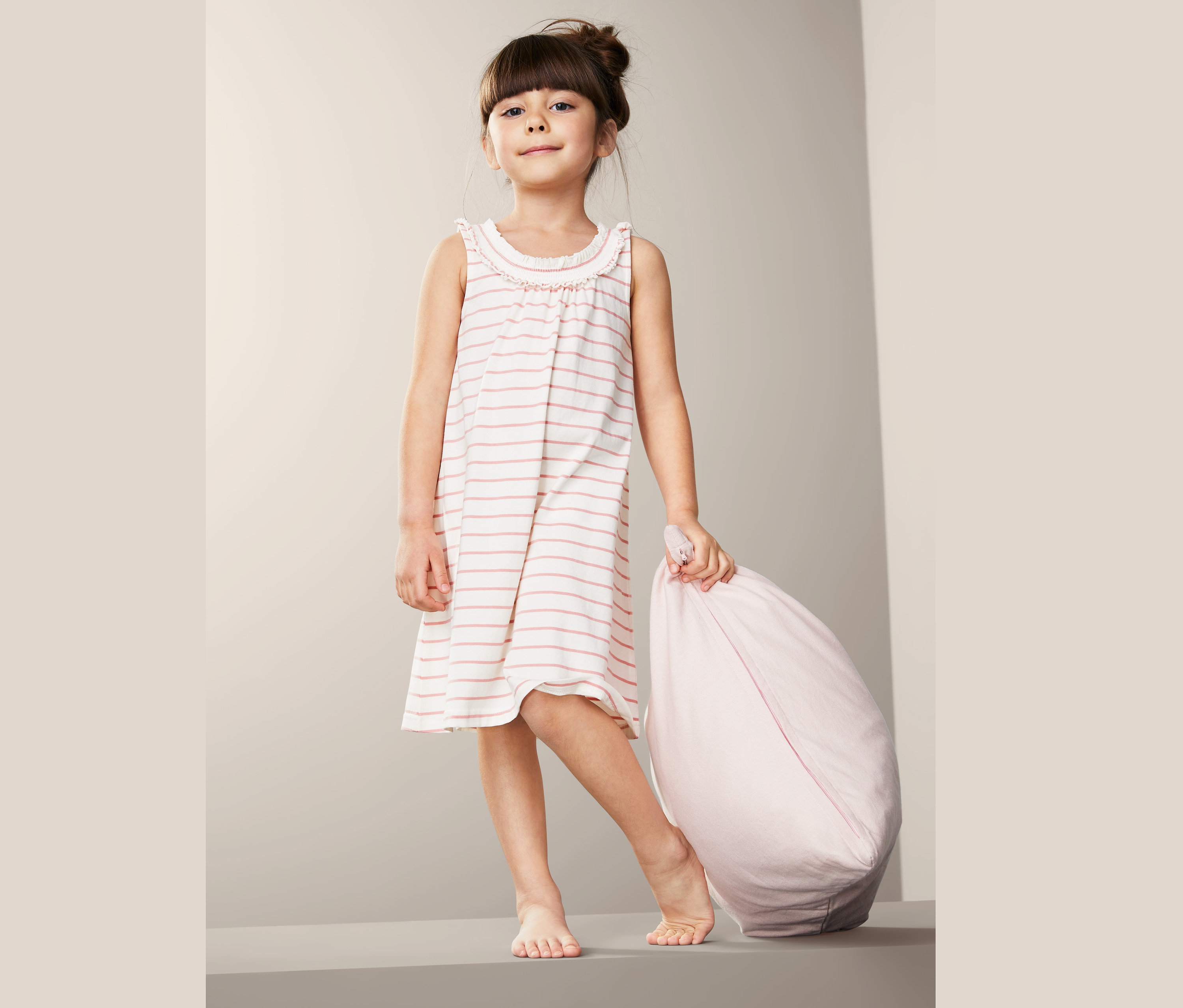 Dievča v bavlnenej nočnej košeli (2 ks) drží ružový vankúš.