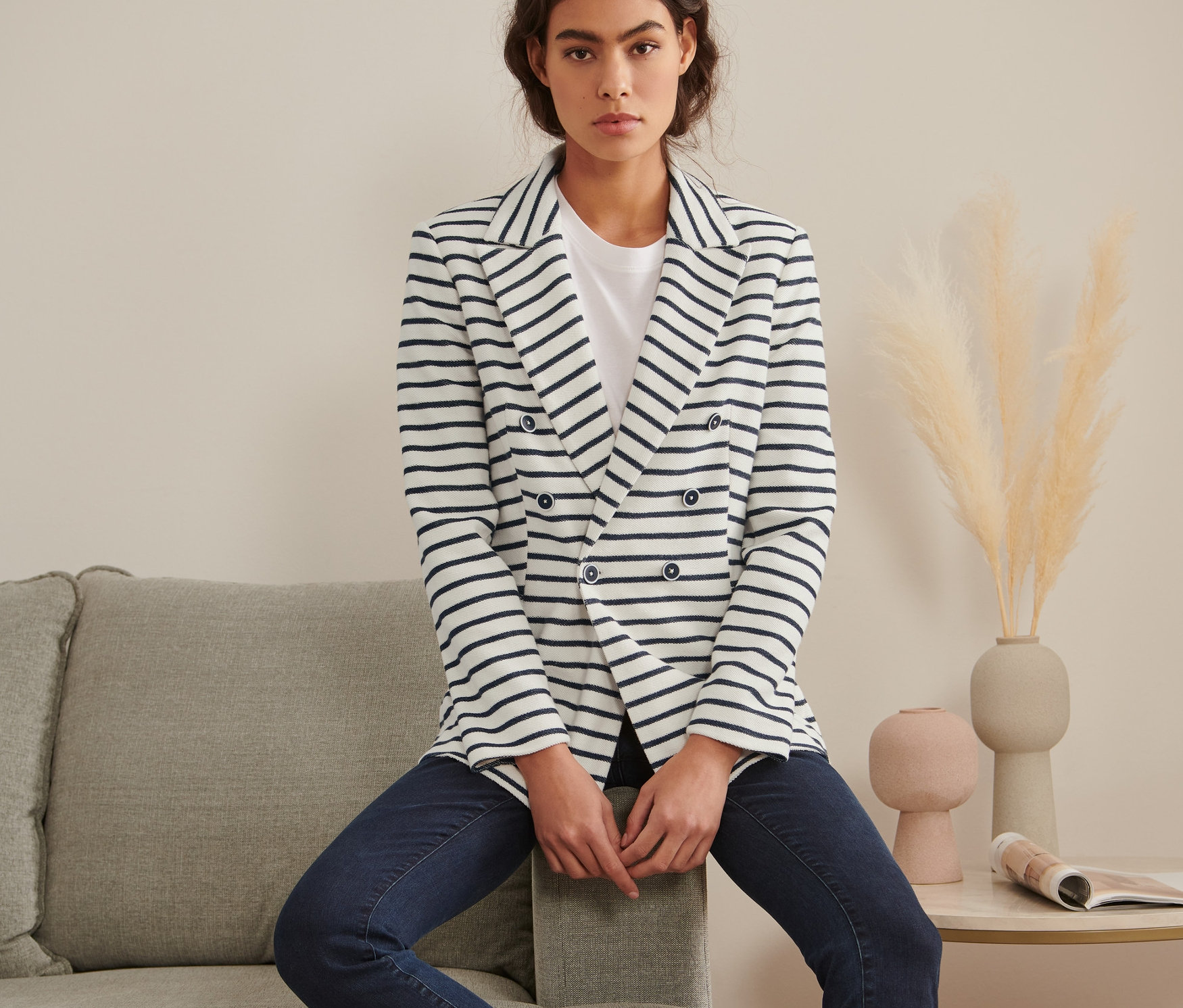 Žena sedí na sivej sedačke a má na sebe prúžkované sako z teplákoviny.