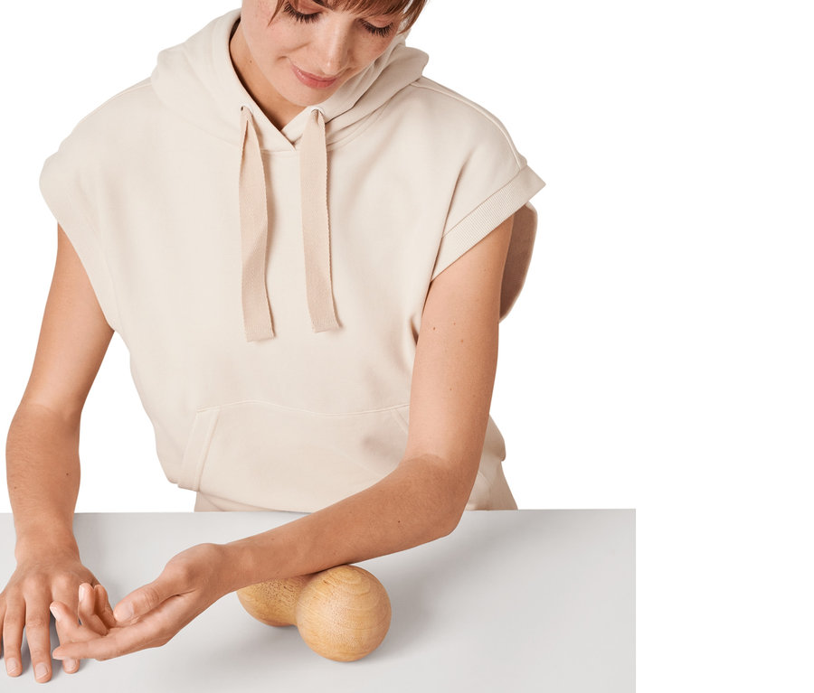 Žena používa dvojitú masážnu loptičku z dreva na svojom predlaktí.