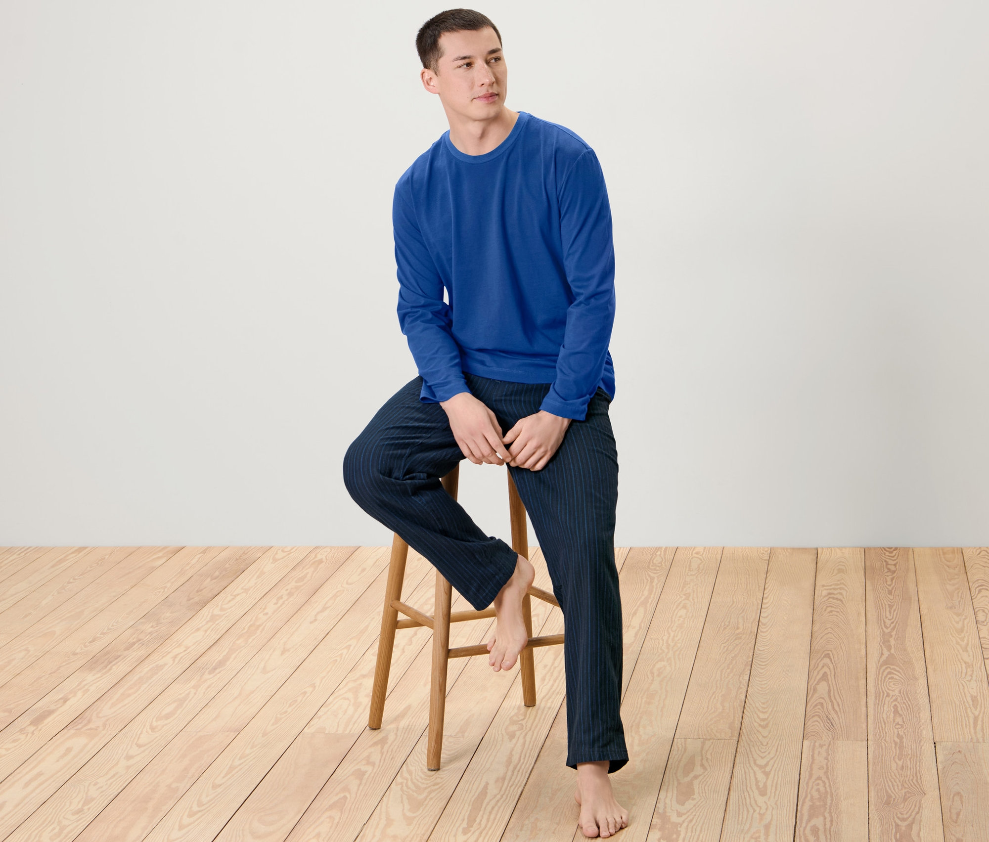 Muž sedí na drevenej stoličke a má na sebe pánske pyžamo s flanelovými nohavicami.