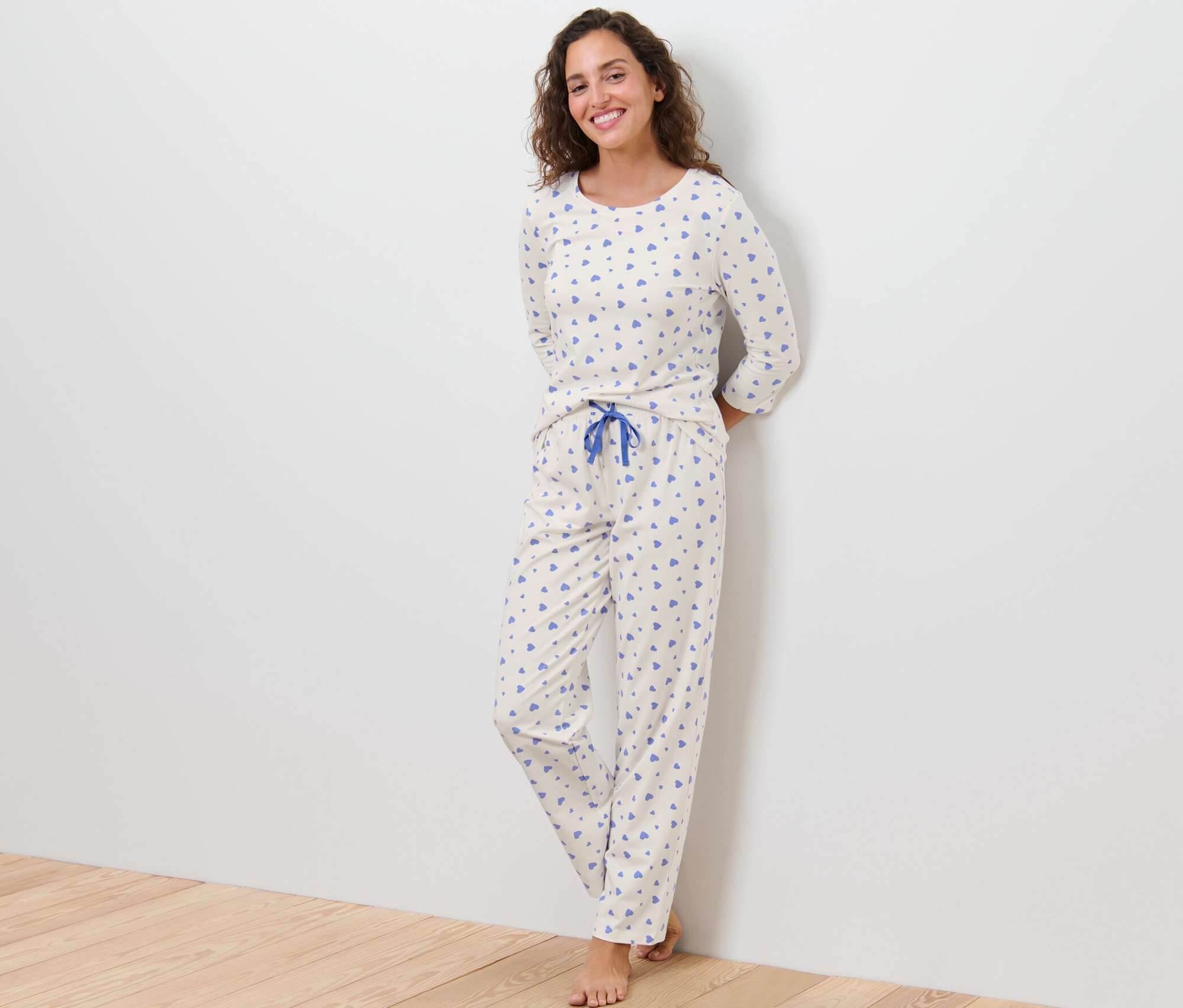 Žena stojí opretá o stenu a má na sebe pyžamo so srdiečkami.