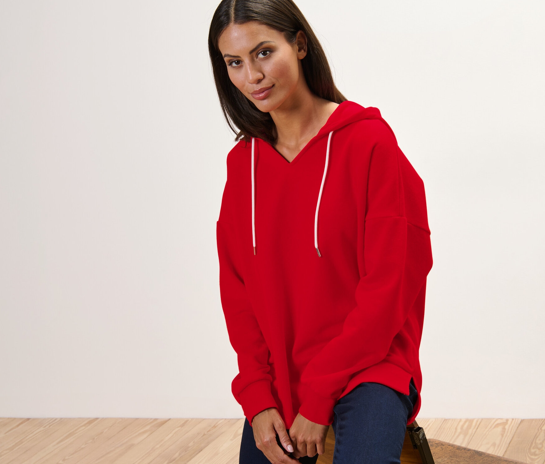 Žena sedí na stoličke a má na sebe červenú mikinu s kapucňou.