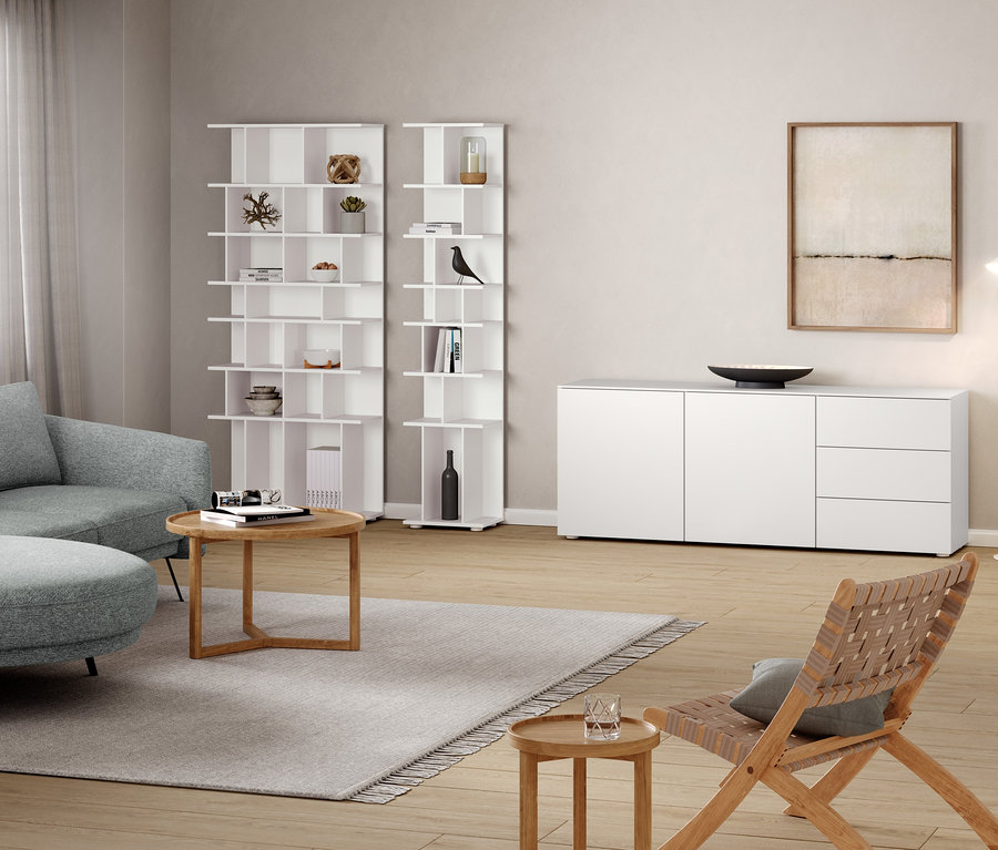 Obývacia izba so sivou pohovkou, okrúhlym konferenčným stolíkom, odkladacou skrinkou, regálom so šírkou cca 80 cm a bielou kovovou stojacou lampou »Cale«.