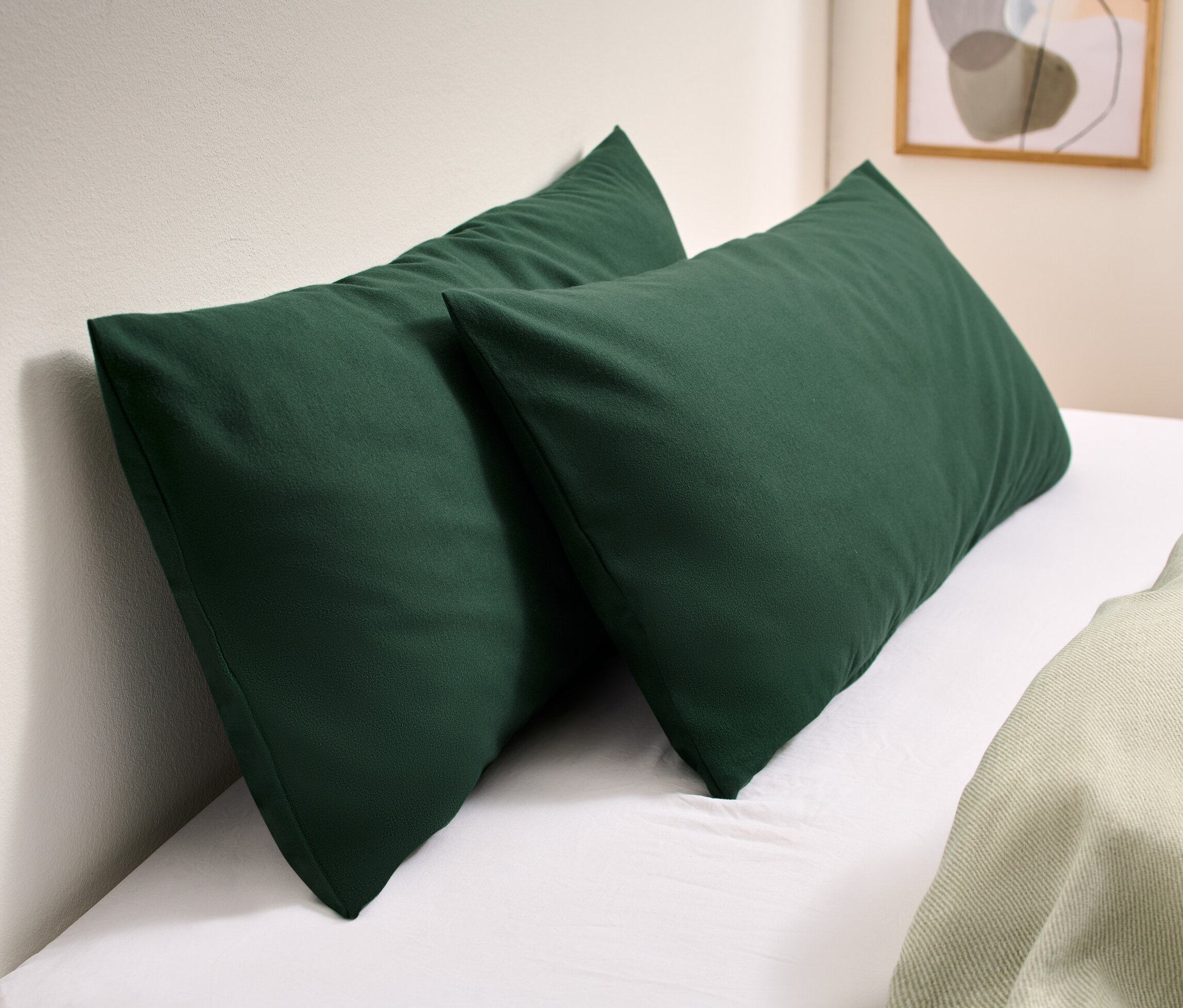 Dve zelené flanelové obliečky na vankúše ležia na bielej posteli.