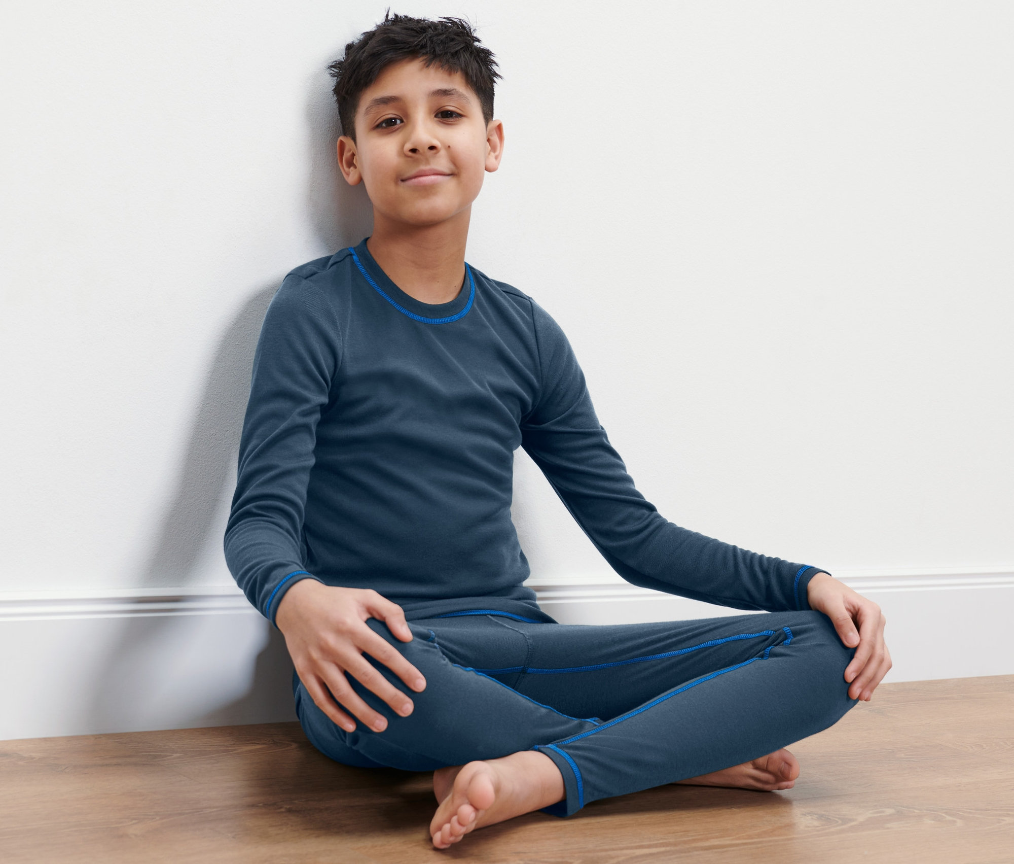 Chlapec sedí na podlahe v detskej lyžiarskej a zimnej spodnej bielizni.