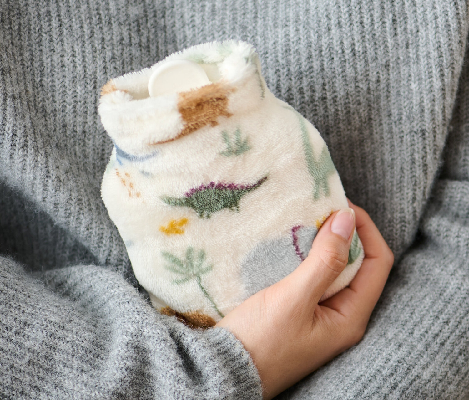 Osoba v sivom svetri drží malý termofor.