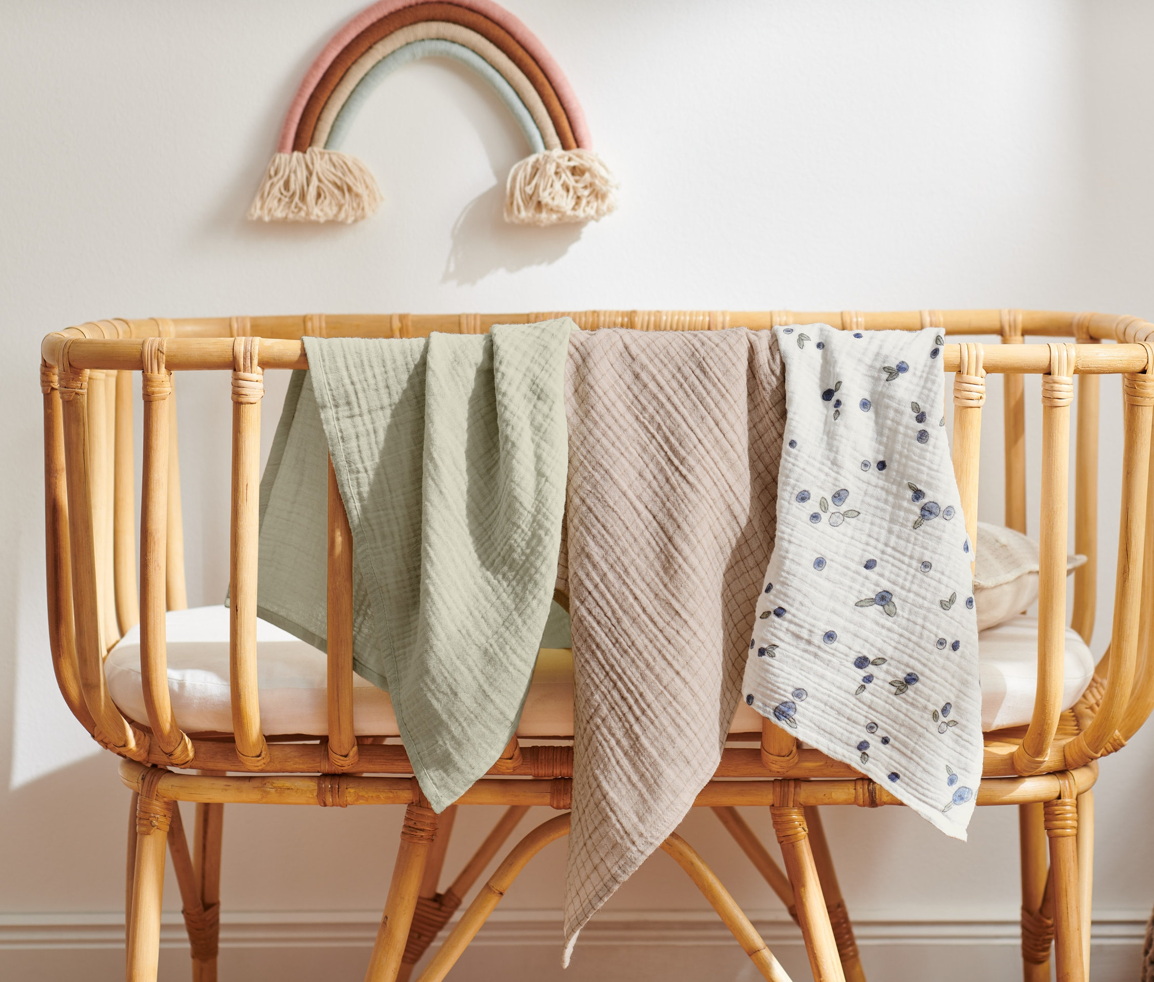Tri mušelínové uteráky pre bábätká prehodené cez postieľku.