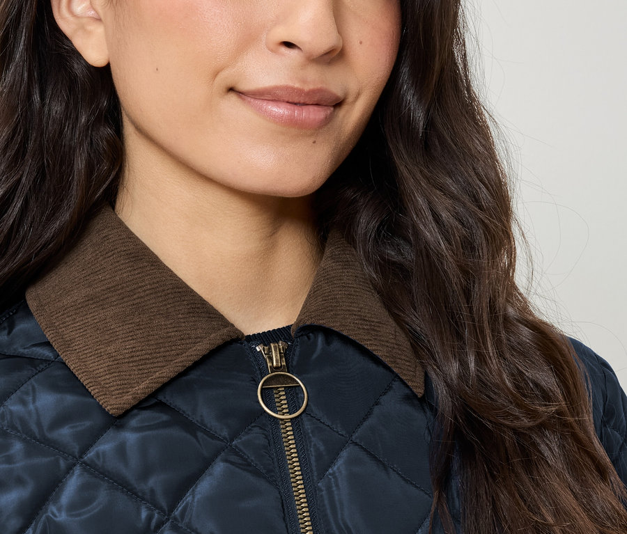 Detail dámskej prešívanej bundy s hnedým menčestrovým golierom a zlatým zipsom.