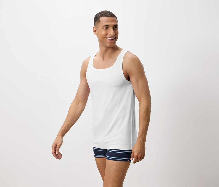 Muž sa usmieva a má na sebe biele tielko a modré pruhované boxerky.