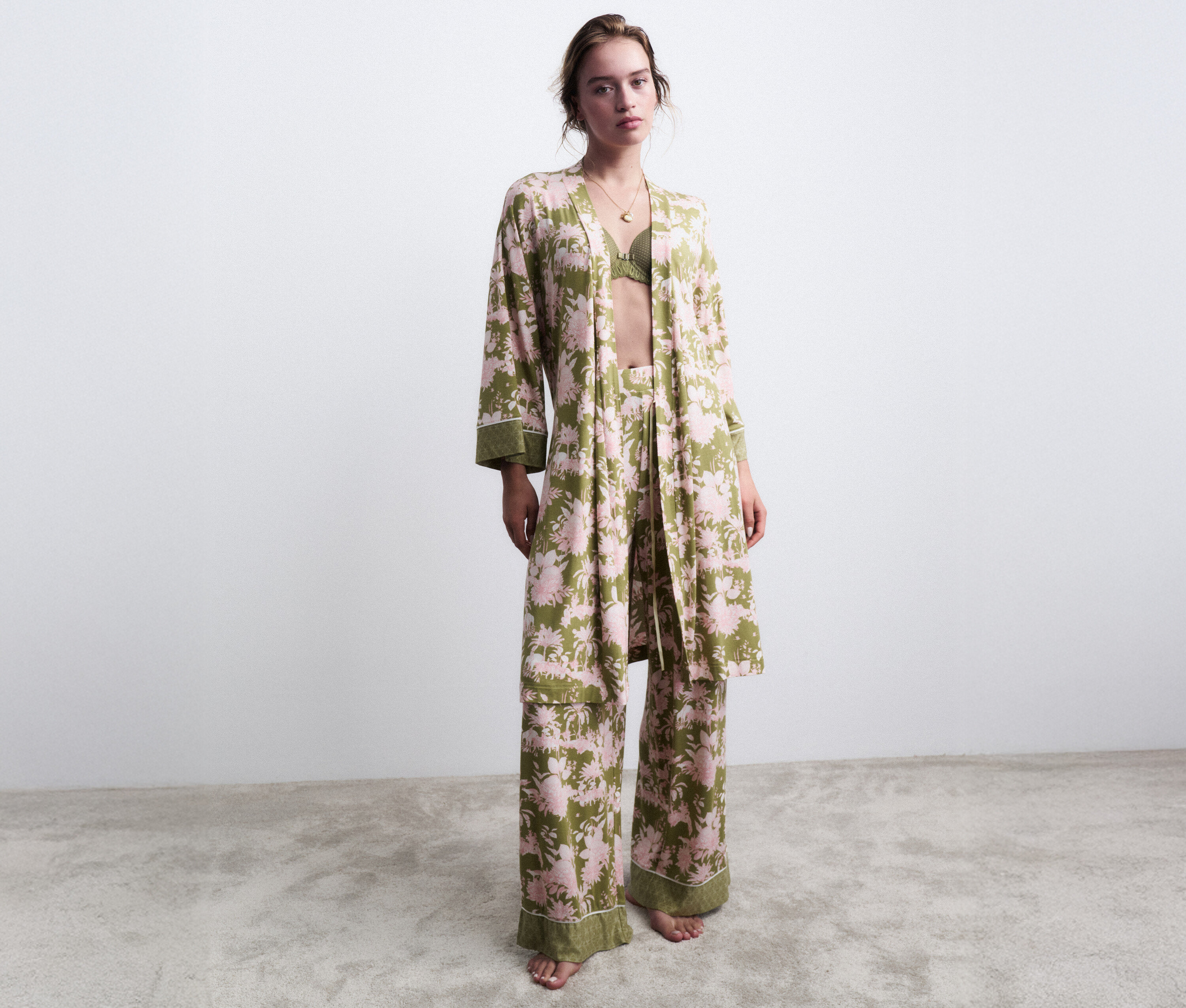 Žena stojí naboso v zelenom pyžame s kvetinovým vzorom a zodpovedajúcim županom.