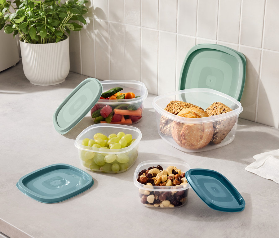 Na kuchynskej linke sú štyri priehľadné nádoby s modrozelenými viečkami, naplnené hroznom, nakrájanou zeleninou, orechmi a sušienkami.