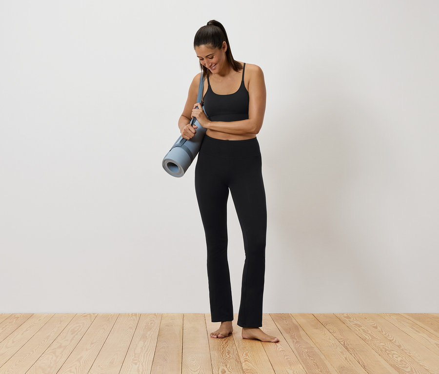 Žena v čiernom športovom oblečení drží podložku na cvičenie.