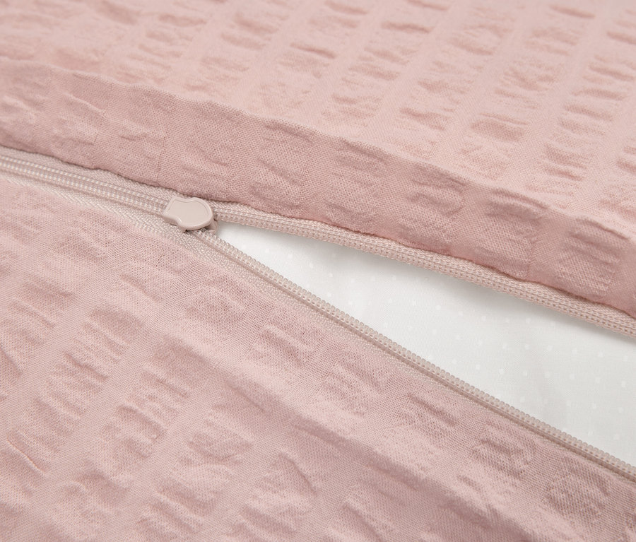 Detail ružového obliečky na prikrývku s textúrou a zipsom, čiastočne odhaleným bielym vnútrom.