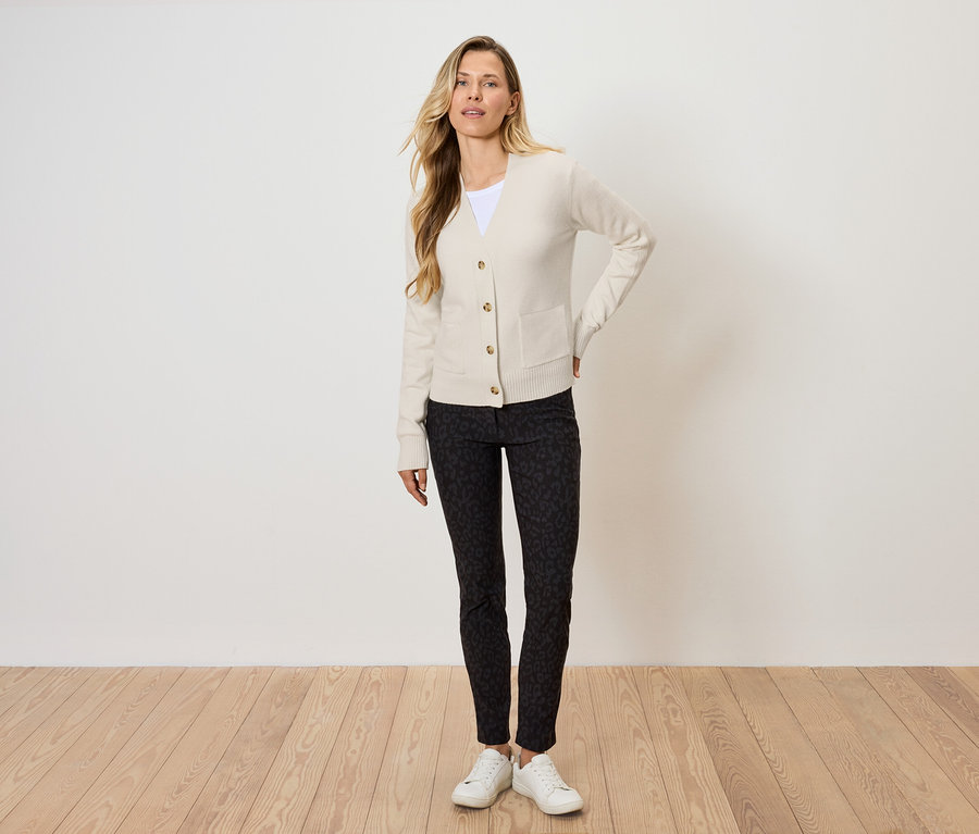 Blondínka pózuje v krémovom kardigáne, čiernych vzorovaných nohaviciach a bielych teniskách.