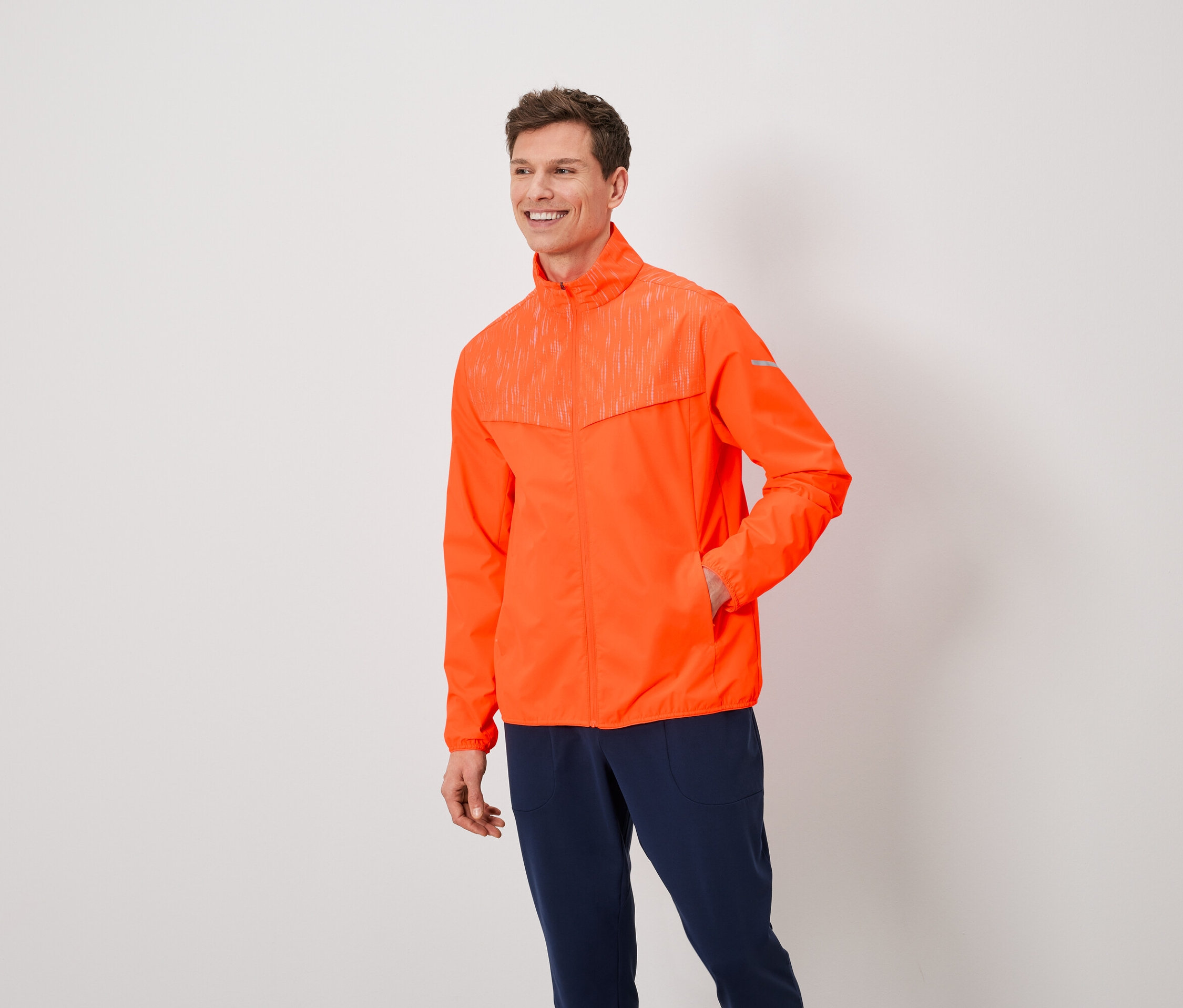 Muž s hnedými vlasmi má na sebe oranžovú bundu a tmavomodré nohavice.