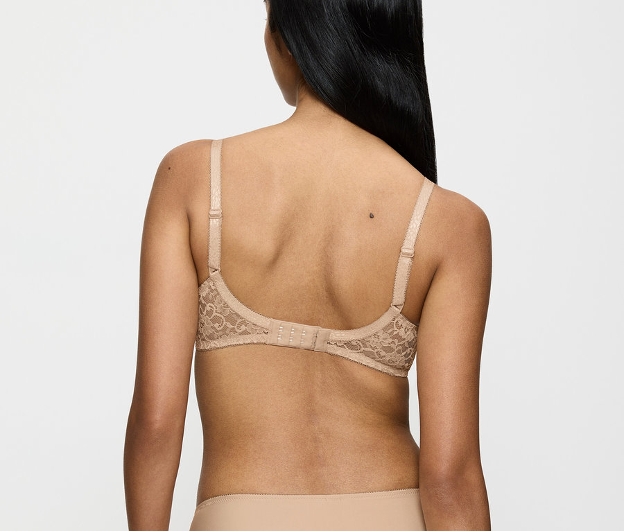 Zozadu je vidieť žena s dlhými čiernymi vlasmi v béžovej čipkovanej podprsenke a nohavičkách.