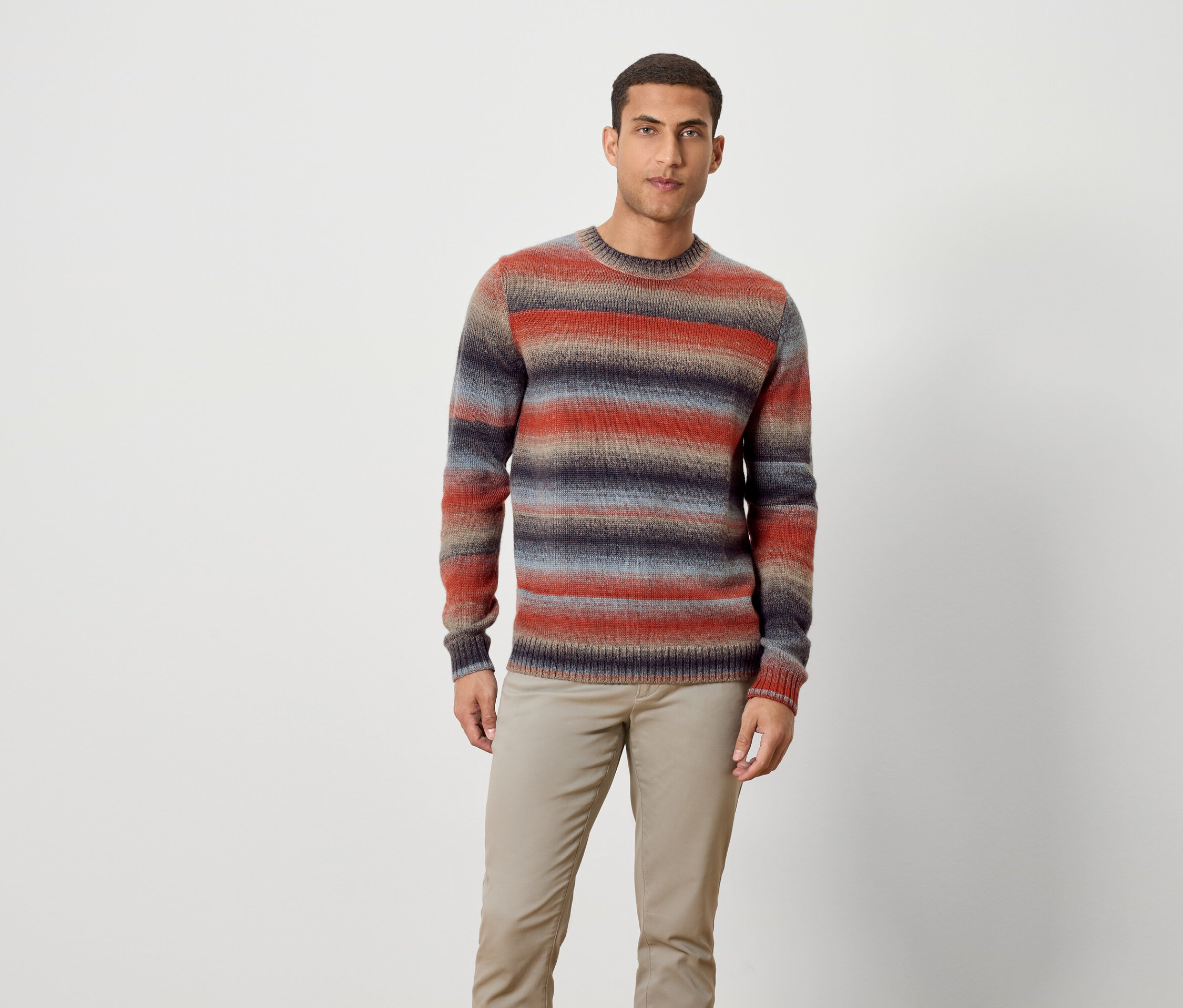 Muž stojí a má na sebe pruhovaný sveter a nohavice.