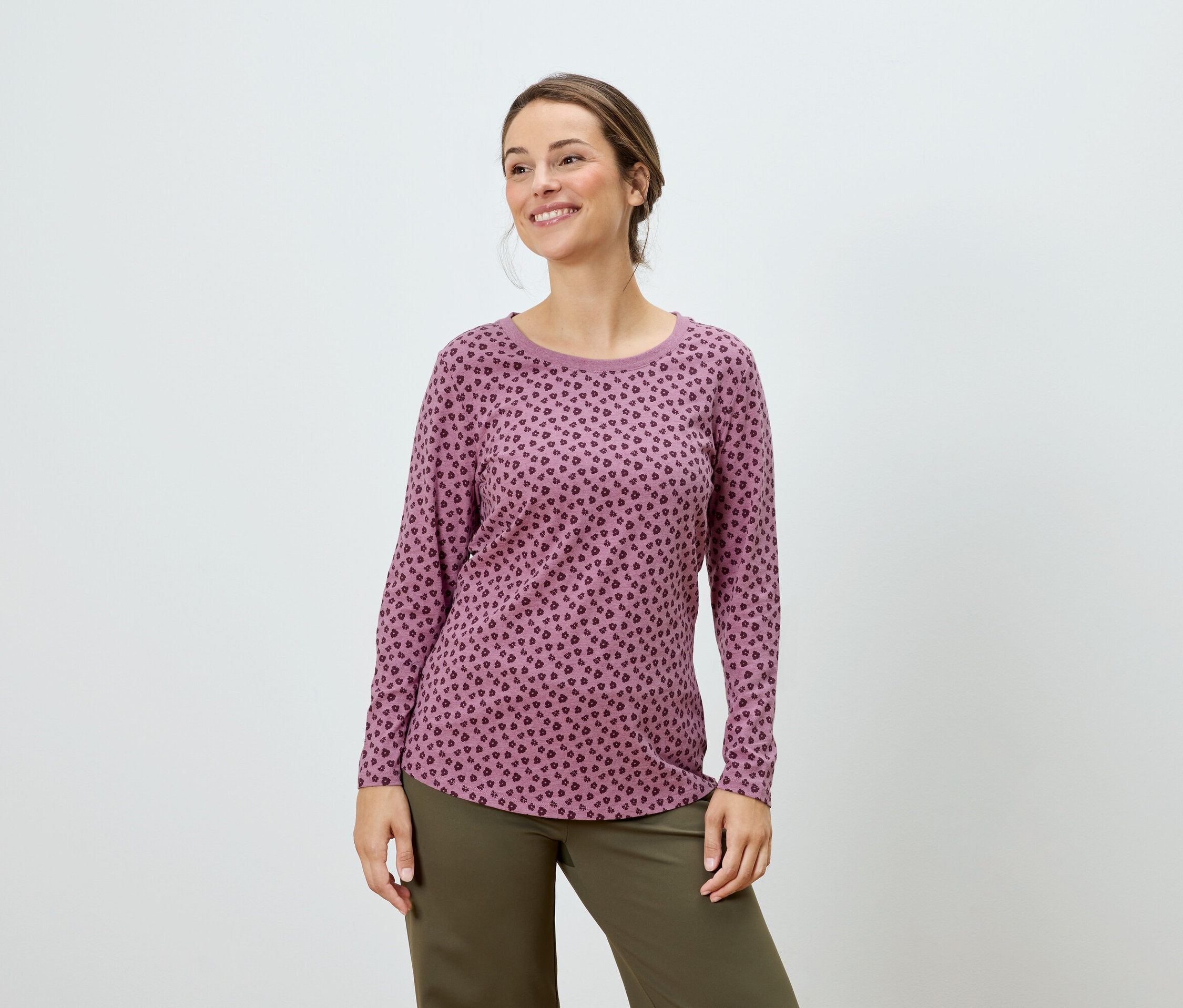 Žena pózuje v ružovom tope s dlhým rukávom a zelených nohaviciach.