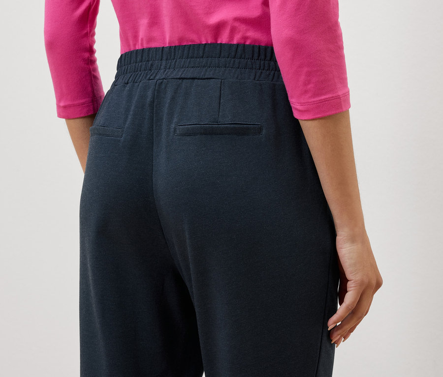 Detailný záber na zadnú časť ženy v tmavomodrých nohaviciach a ružovej blúzke.