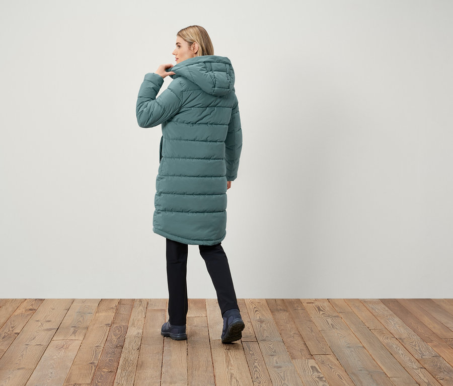 Žena v dlhej prešívanej bunde s kapucňou, chrbtom k kamere.
