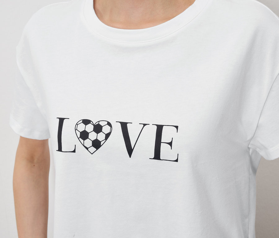 Detailný záber na osobu v bielom tričku s nápisom „LOVE“, kde je písmeno „O“ nahradené srdcom v tvare futbalovej lopty.