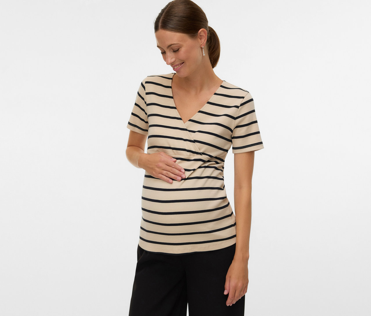 Žena s konským chvostom má na sebe tehotenské tričko MAMALICIOUS »MLLANE TESS« s pruhmi a čierne nohavice, pričom sa dotýka brucha.