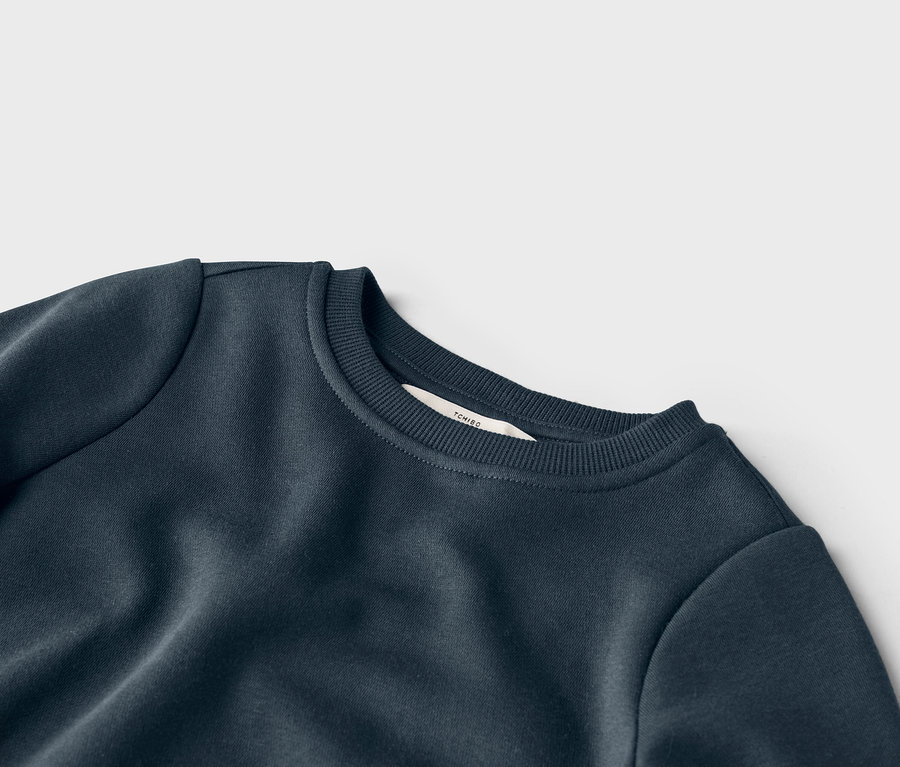 Detailný pohľad na námornícke modrú mikinu s okrúhlym výstrihom a štítkom značky Tchibo na golieri.