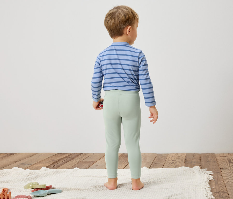 Dieťa stojí chrbtom k fotoaparátu, má na sebe modro pruhovanú košeľu a svetlozelené legíny.