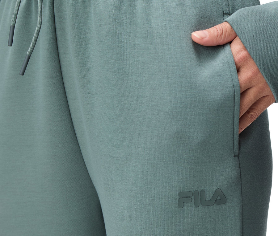 Detailný záber na osobu v zelených teplákoch Fila s elastickým pásom a šnúrkou a rukou vo vrecku.