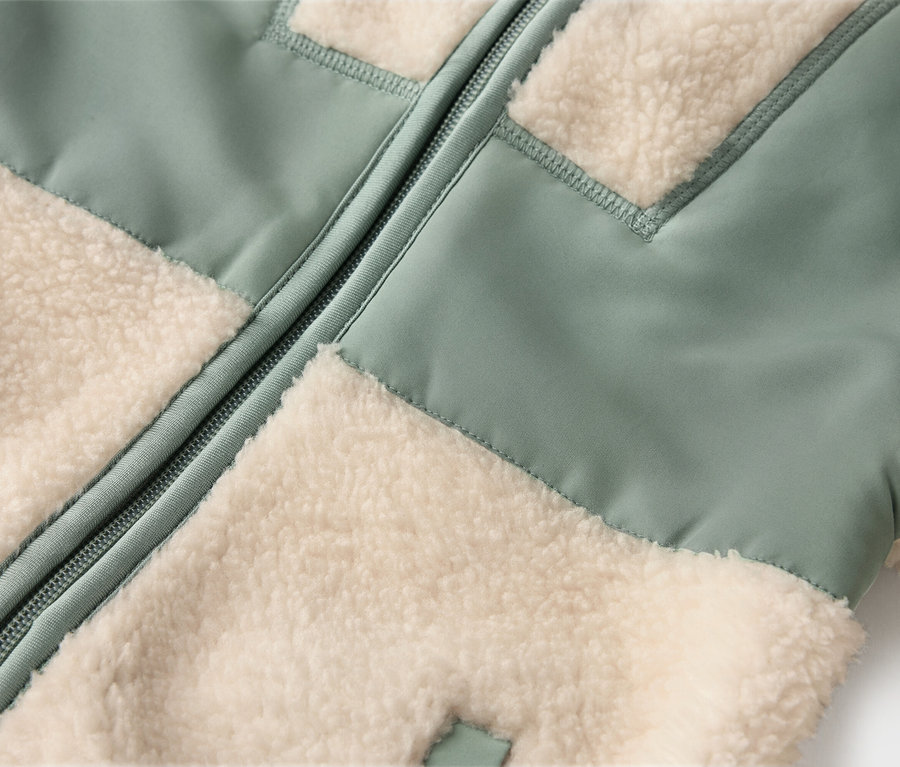 Detail bundy so svetlozelenými a krémovými flísovými panelmi a zipsom v strede.