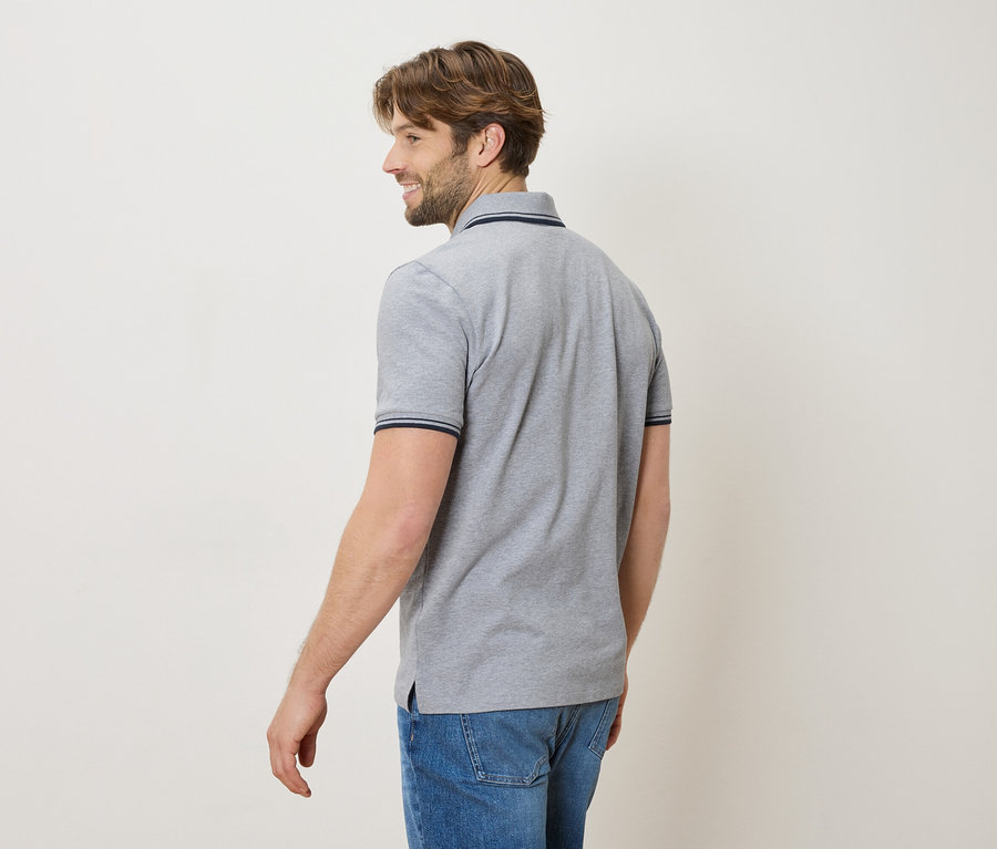 Muž zozadu v sivom polo tričku a džínsoch, usmievajúci sa.