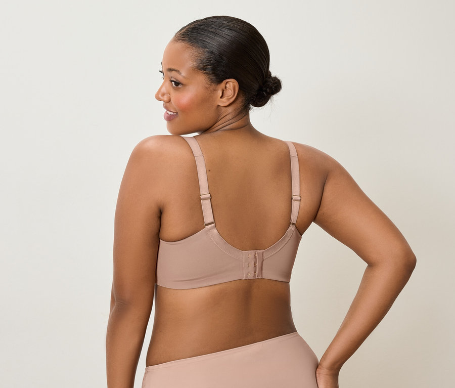 Pohľad zozadu na ženu tmavej pleti s drdolom, ktorá má na sebe telovú podprsenku a ladiace spodné prádlo a pozerá sa cez plece doľava.