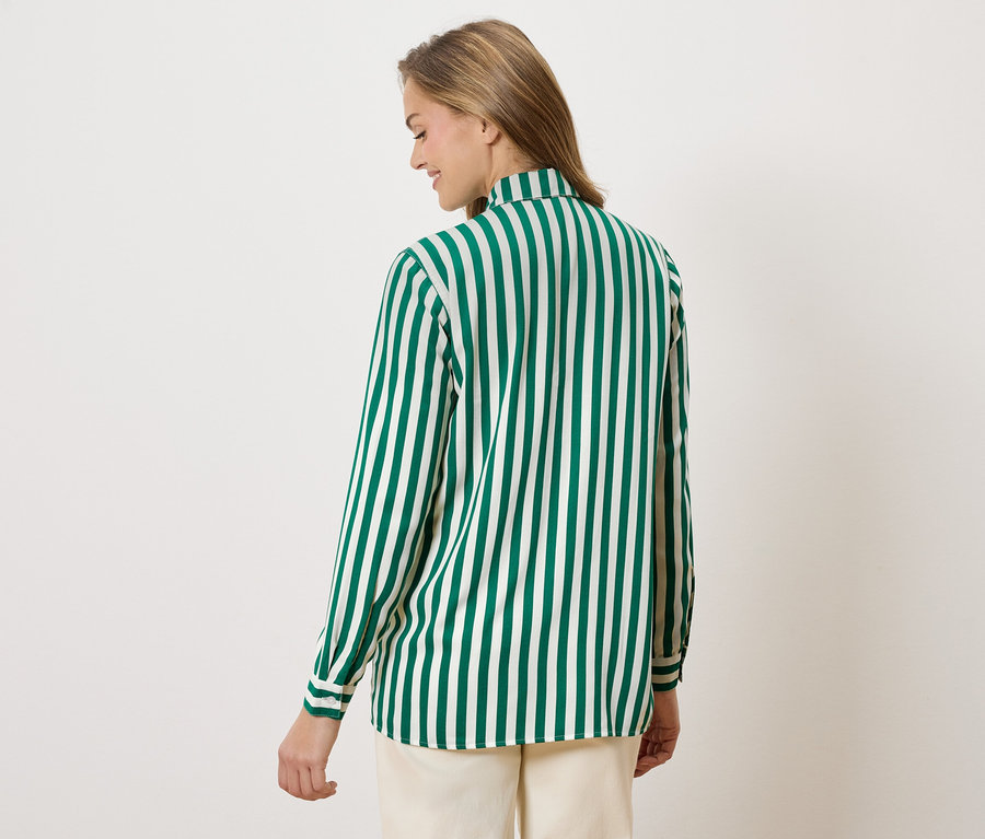 Žena zozadu v zeleno-bielej pruhovanej blúzke a béžových nohaviciach.