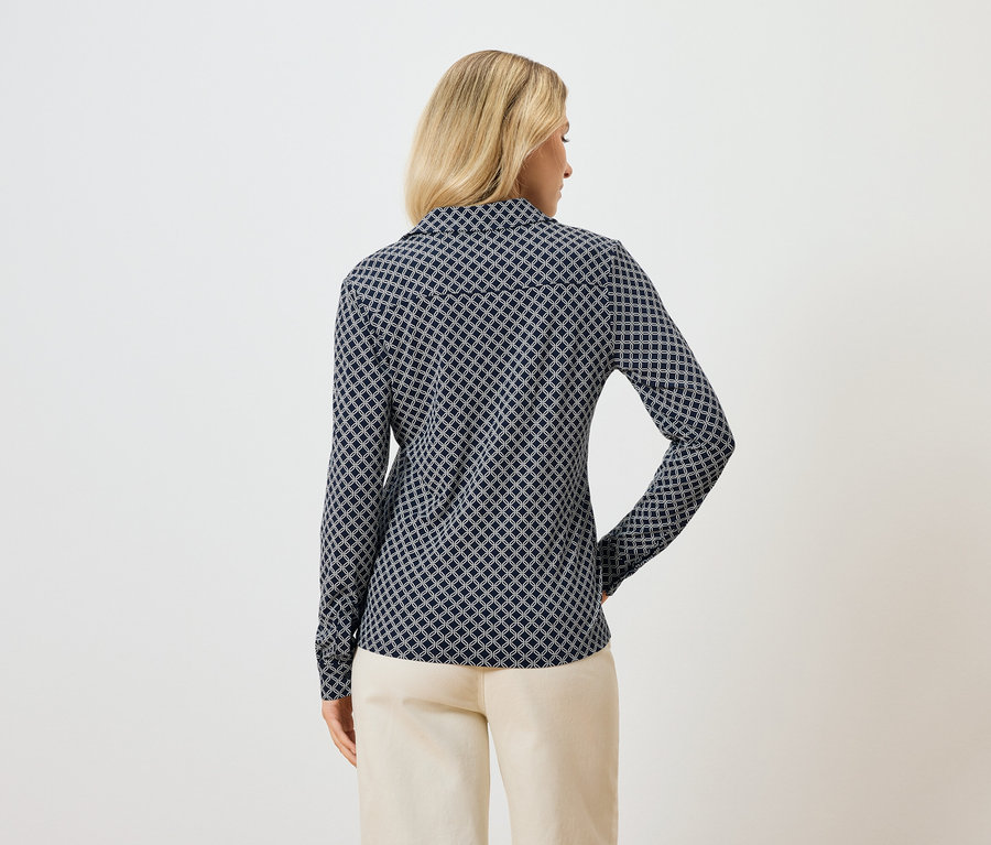 Pohľad zozadu na blondínku v modrej vzorovanej blúzke s dlhým rukávom a svetlých nohaviciach.