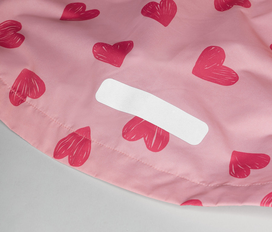 Detail ružovej látky so vzorom srdca a bielym štítkom.